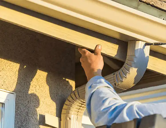 Person installing or repairing a gutter system on the side of a house using both hands.