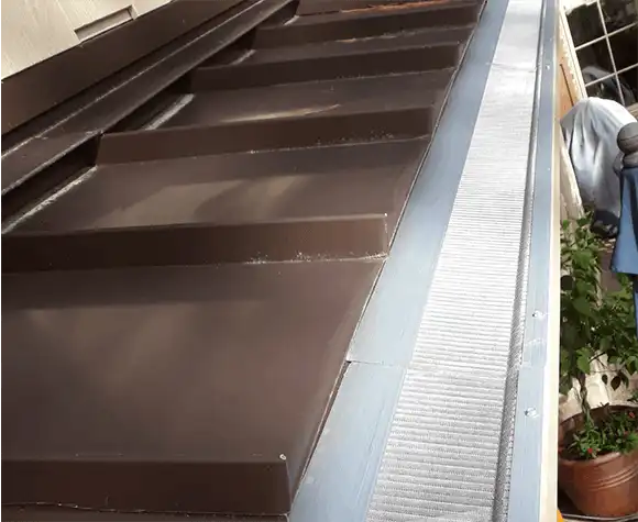 Close-up view of a brown metal roof with a silver gutter guard installed along the edge.