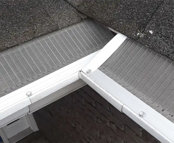 Close-up view of a house roof corner with metal mesh gutter guards installed over the rain gutters.