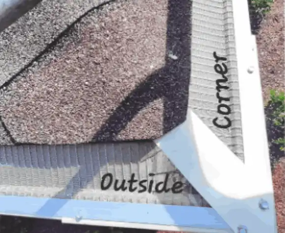 A white rain gutter piece labeled "Outside Corner" is installed on a roof with brown shingles.