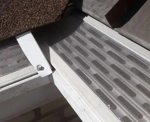 Close-up of a metal gutter guard installed on a roof, showing mesh screen and roofing materials.