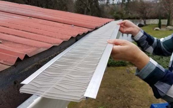 A person installs a metal mesh guard on a roof gutter to prevent debris from entering.