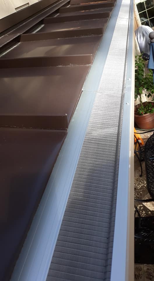 Close-up view of a house roof with a brown metal surface and a silver mesh gutter guard installed.