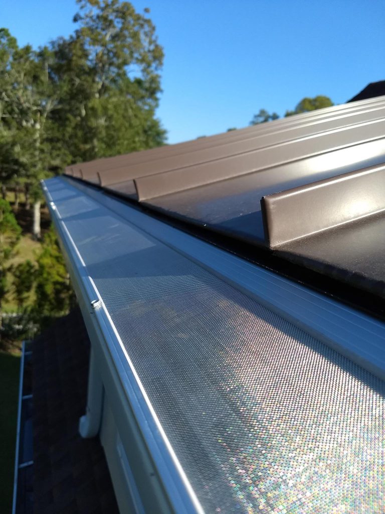 Close-up view of a metal roof with brown panels and a mesh gutter guard installed along the roof edge.