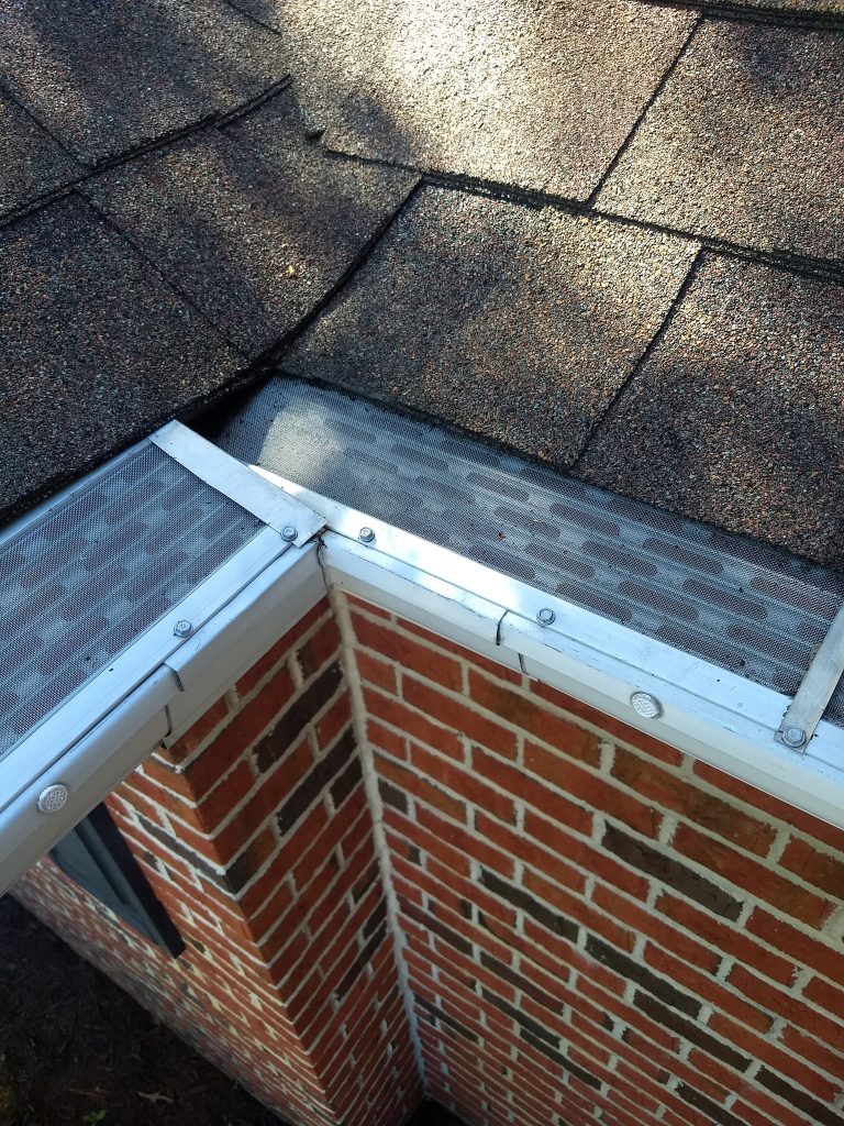 Close-up of a brick house's roof corner with a metal gutter guard covering the rain gutter.