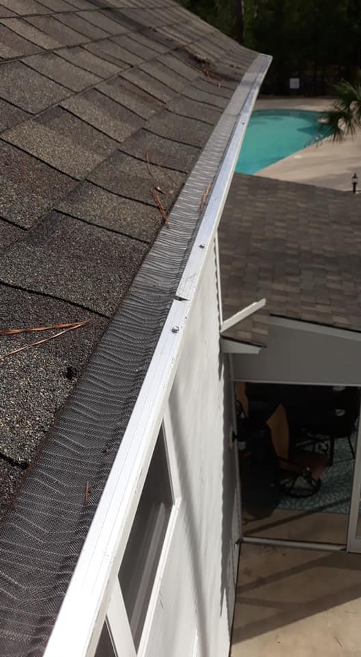 Close-up view of a house roof with gutter guards installed, showing a few pine needles on the roof near a pool area.