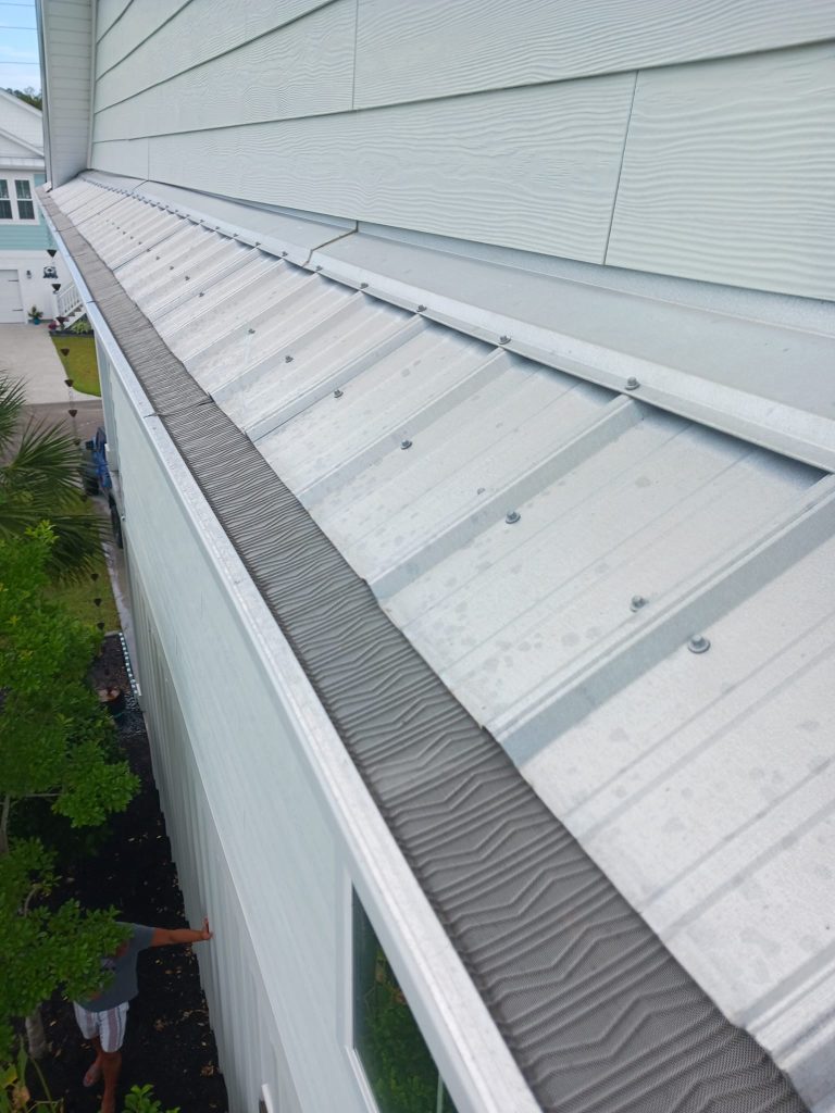 A close-up view of a metal roof with mesh gutter guards installed along the edge of a two-story building.